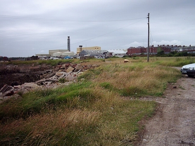 scruffy wasteland in the foreground with large industrial units in the background
