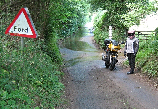 My motorbike and the girlfriend next to a damp road, and a ford sign