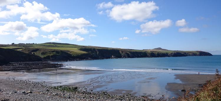 Abereiddy Beach, stones and pebble lead to sand and the sea between outcrops