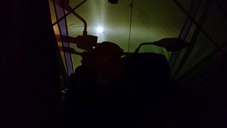 A bright eerie light outlines a motorcycle against the material of the tent.