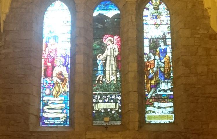 3 narrow arched windows filled with stained glass images at Dornoch Cathedral