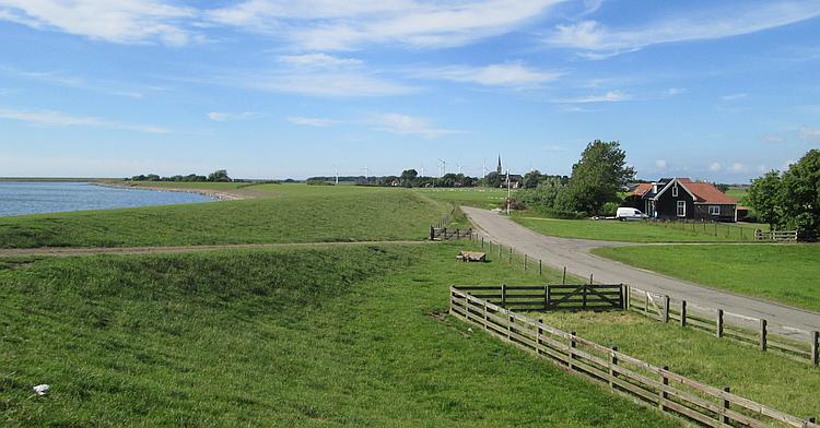 A typical dutch dyke with a large body of water to one side and flat lush green farmland on the other