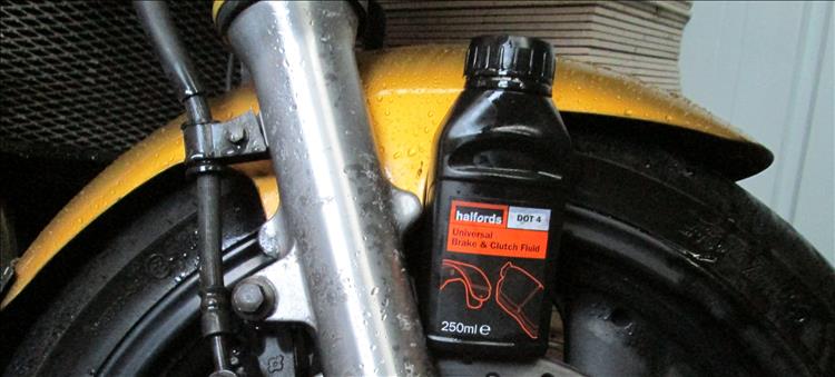 A bottle of Halfords brake fluid perched on a motorcycle wheel
