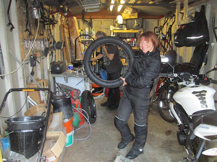 A garage filled with tools, shelves and equipment and Sharon holding a tyre