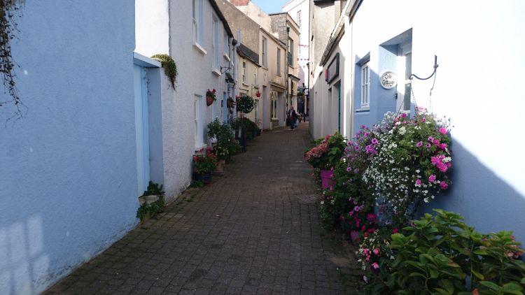 light blue and white painted houses line a narrow street highlighted with sun