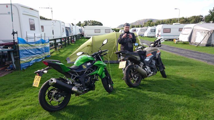 Ren is stood outside the tent taking pictures surrounded by caravans and the motorcycles