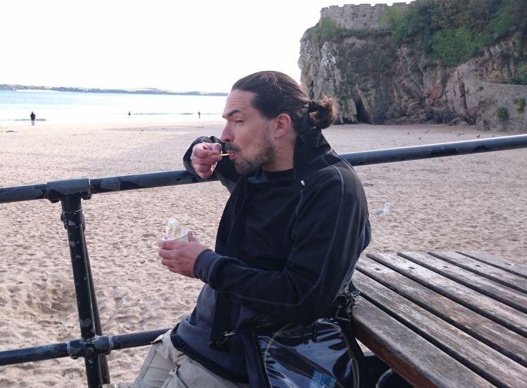 Ren is greedily shovelling ice cream into his face with the beach behind him at Tenby