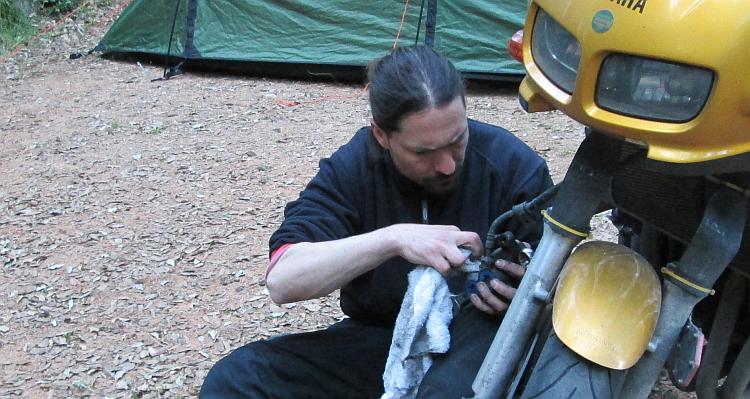 Ren looks intensely at the brake calliper he's working on at a campsite