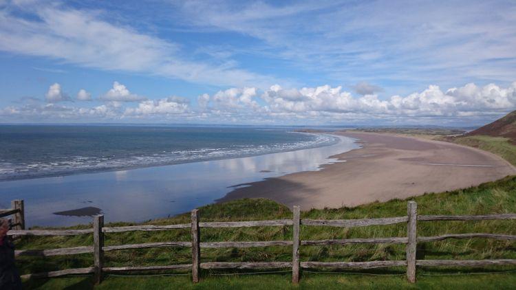 Seen from the bluff above, Rhossili beach stretches out into the distance with blue skies