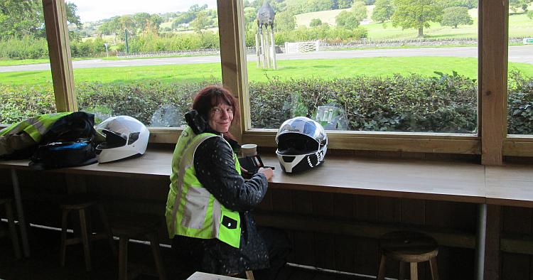 Sharon drinking tea and smiling at the camera surrounded by bike gear