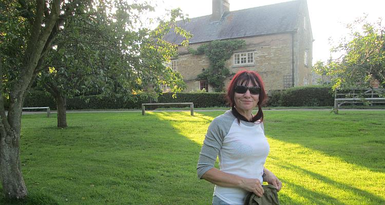 Sharon smiles wearing her sunglasses with a stone farmhouse behind her at the campsite