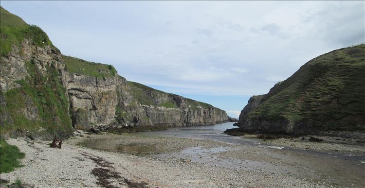 A cove with steep rocky sides and a small river running across pebbles to the sea
