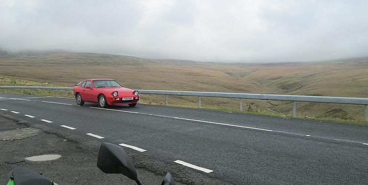 An old red Porsche crosses the misty moors and hills of the pass, quite safely