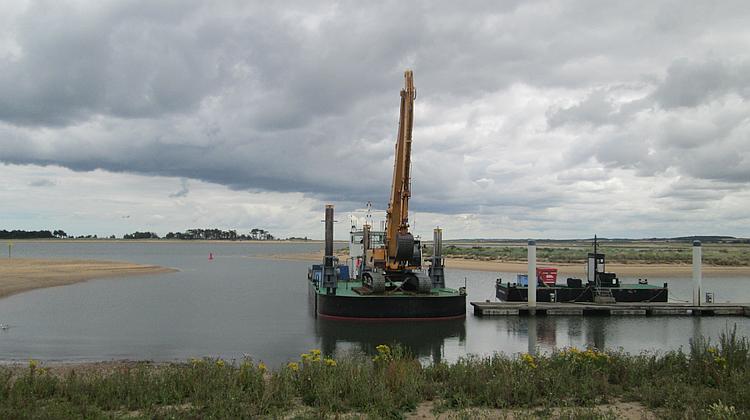 A large tracked excavator on a barge at Wells-next-the-sea.