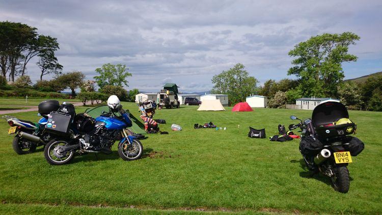 Motorcycles are having tents and gear fixed onto them in the sun at the campsite in Applecross