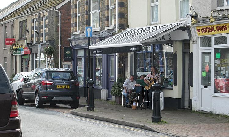 A couple play guitar and sing outside a small shop at Ystradgynlais