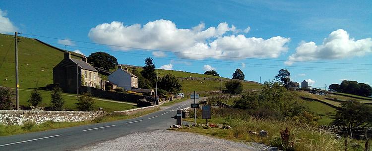 A delightful road twists past some stone houses in the Dales countryside