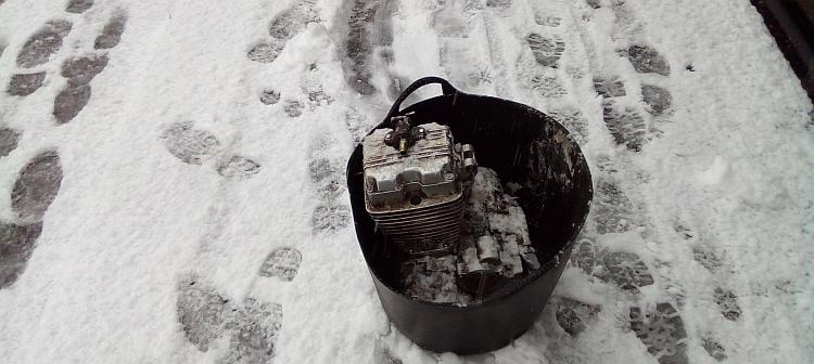 The 125 engine is in a black rubber bucket on a snow covered footpath