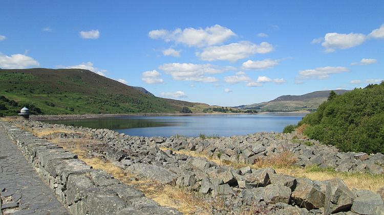 Afon Tryweryn lake is bathed in sun surrounded by green hills and blue skies