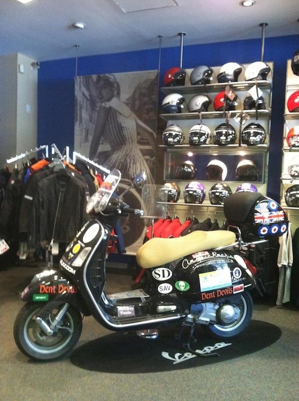 A Vespa scooter covered in sponsor stickers at the shop