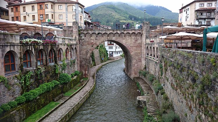 An old ornate stone bridge crosses a river cut deep between the houses and verandas in Potes