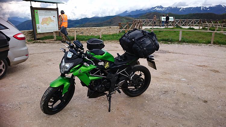 Sharon's 250 with a tourist information board behind then the vast mountains stretch away