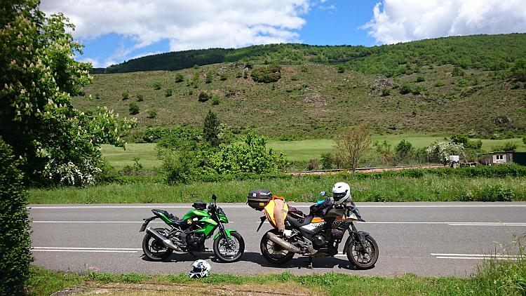 The 250 and 500 parked by the side of the road surrounded by the lush verdant scene