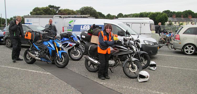 Sharon is smiling at the camera with motorcycles and cars in the queue for a ferry behind her
