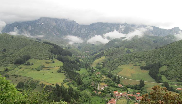 A large green valley with huge rocky and jarring peaks covered in clouds in the distance