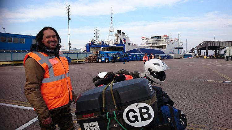 Ren smiles at the camera with his bright hi-viz, the bikes and the ferry in the background
