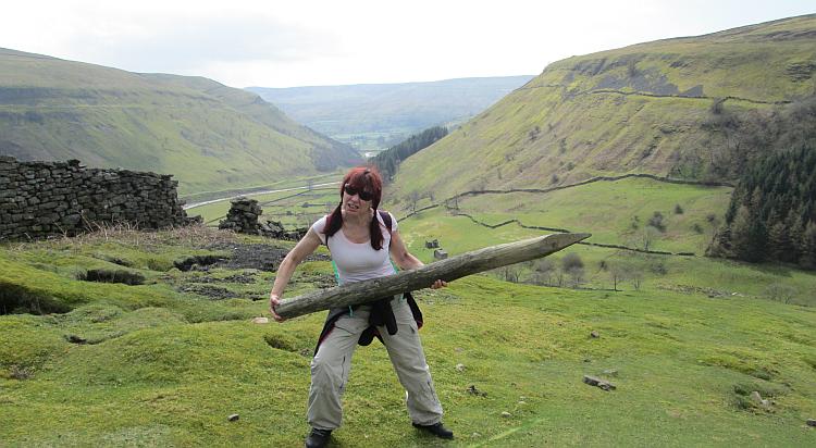 Sharon holds a large wooden stake, a fence pole, looking aggressive against the Dales backdrop