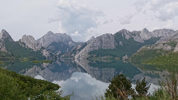 Sharp angular and snow tipped mountains reflected perfectly in the water of a lake in The Picos