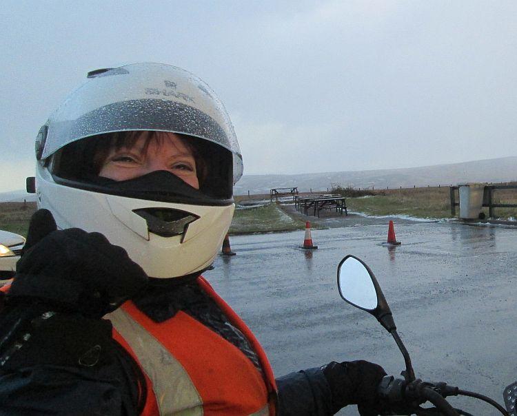 Sharon in her helmet and bike gear on a very very wet day giving a thumbs up and smiling