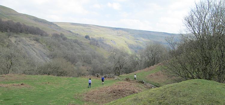Several walkers make their way down a grassy path in the Dales