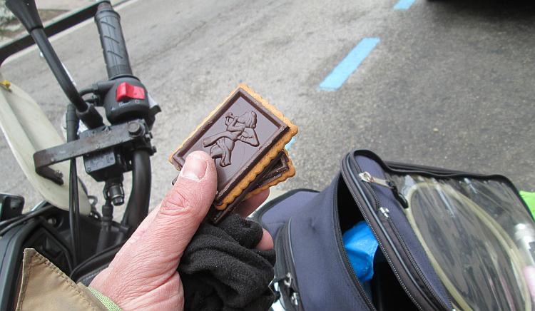 2 biscuits with simple icons in the chocolate covering are held in Ren's hands by the bike