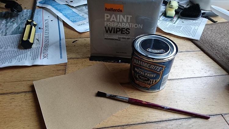 A tin of hammerite, some paint preparation wipes and a small paint brush on Sharon's floor