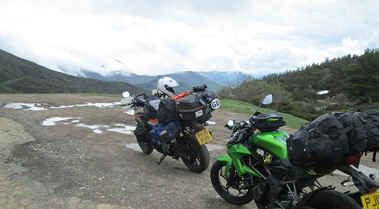 The 2 motorcycles with their camping kit on the peak of the pass, there's a little snow here and there