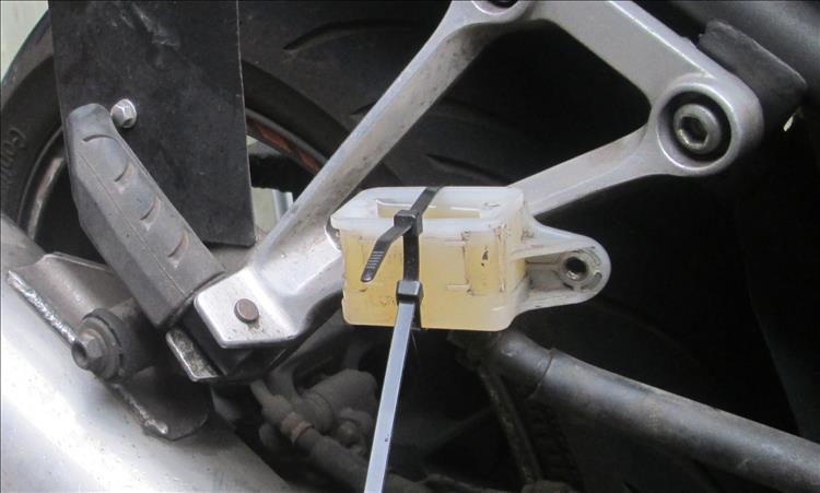 The rear brake fluid reservoir is zip tied onto the rear footrest hander on the Honda