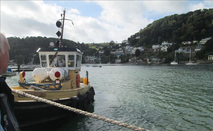 A small tug boat pushes and shoves the pontoon that the bikes are on across the river Dart