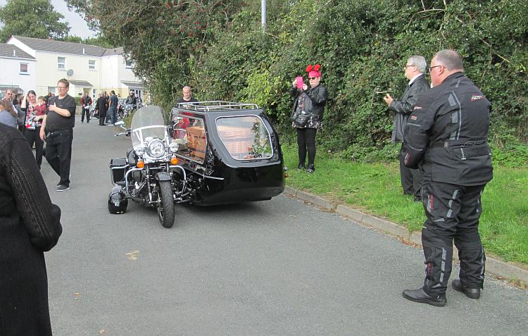A motorcycle and sidecar, with the wicker coffin in the sidecar