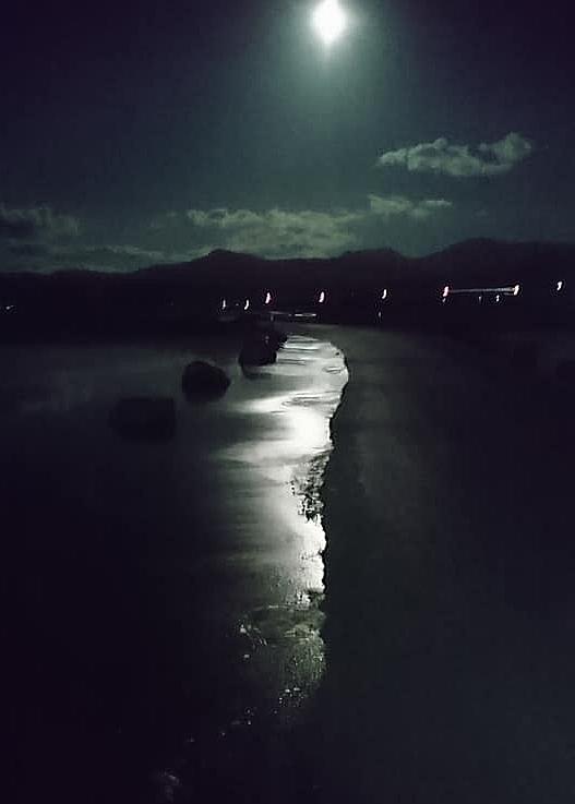 The bright moon illuminates water lapping over the road as the tide comes in