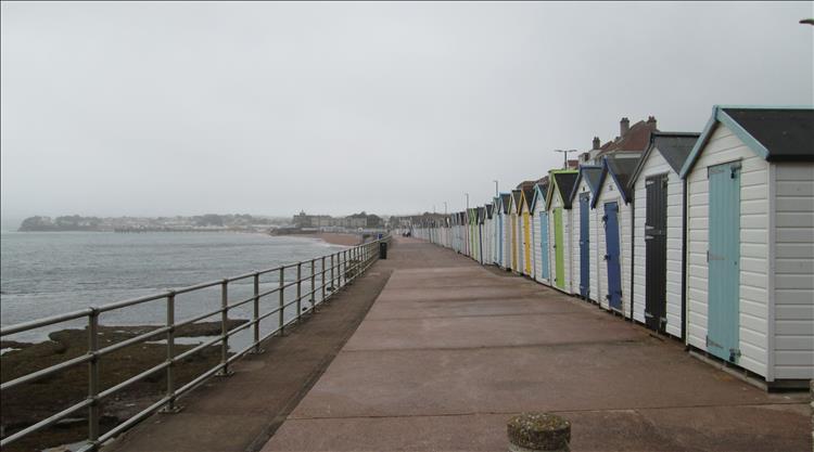 A long line of beach huts by the sea wall at Preston Sands Devon. The weather is still grey
