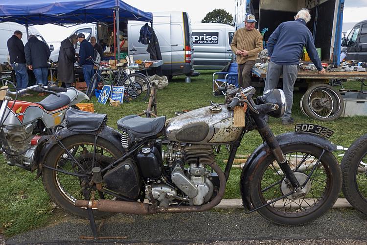 A rusty old Norton motorcycle with a price tag on it for sale outside the show