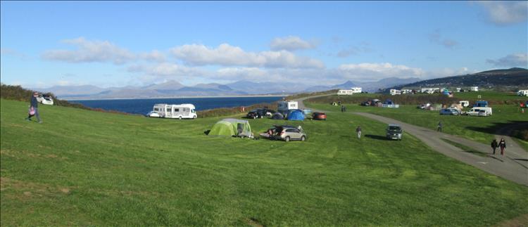 A rolling field with a sprinking of campers, behind the bay and the welsh mountains in the autumnal sun