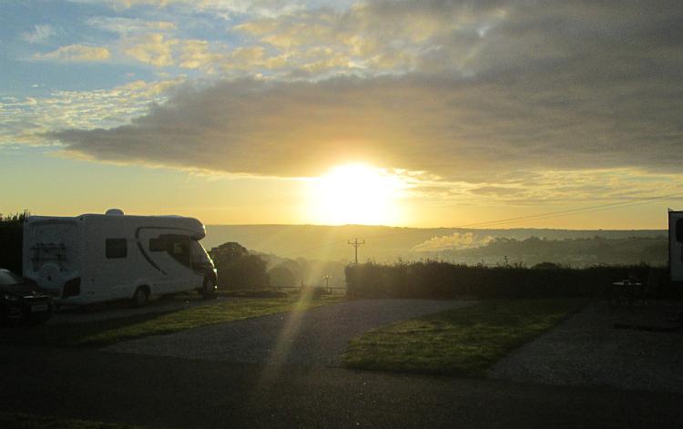 Hazy clouds and light blue skies and the sun look huge as it rises above the Horizon in Cornwall
