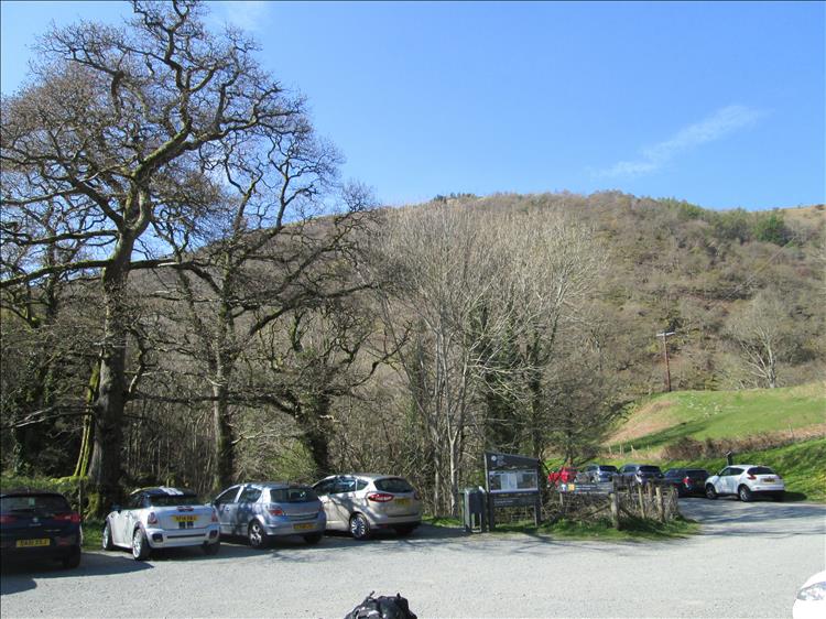 A gravel car park among leafless trees and green hills near Aber Falls