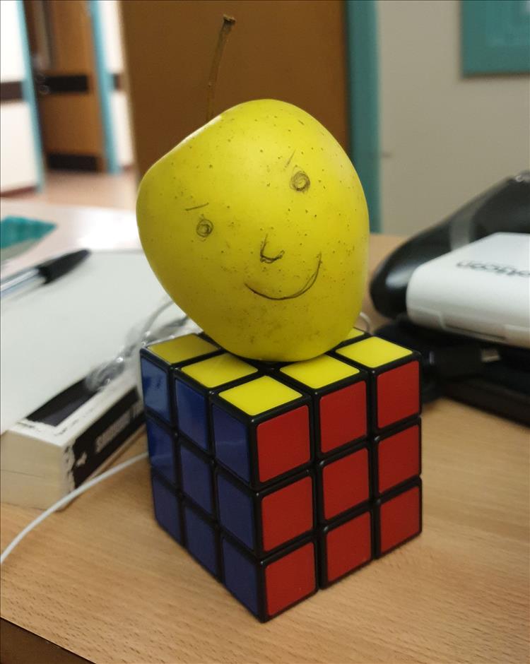 An apple with a face drawn on it placed on a rubik's cube