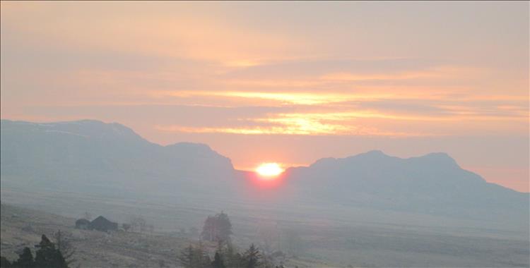 The orange sun rises between two mountain peaks in North Wales Snowdonia