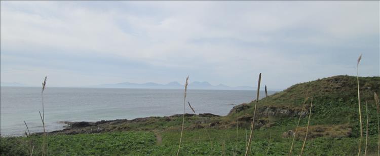 Across hazy waters in the distance the isle of Islay has steep hills pointing up