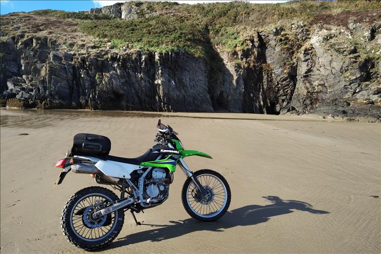 Bob's KLX250 motorcycle set in a beach with steep rocky cliffs
